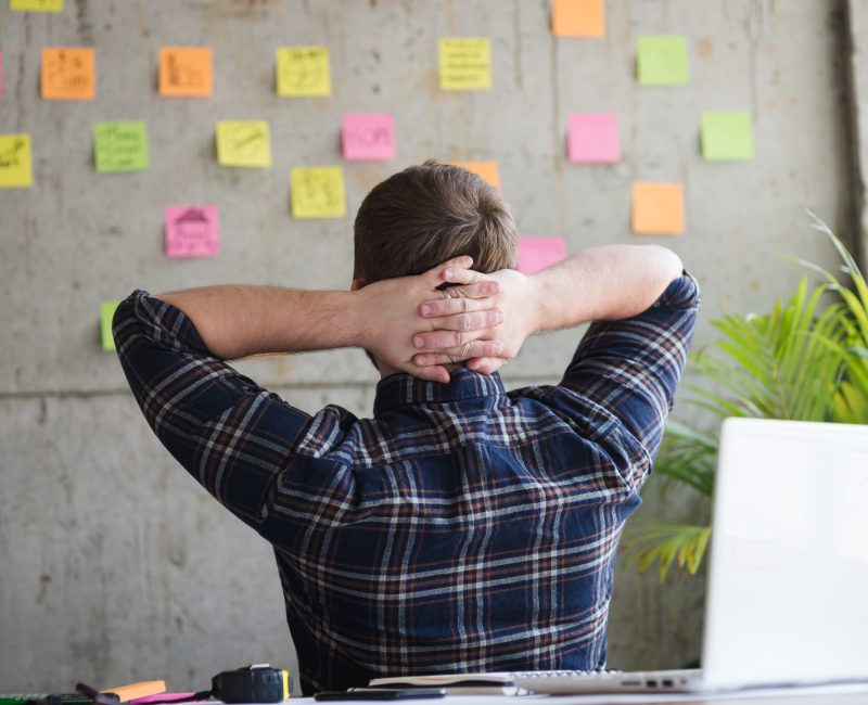Back of entrepreneur sitting in office and look at colorful sticky message on cement wall. Work lifestyle concept.